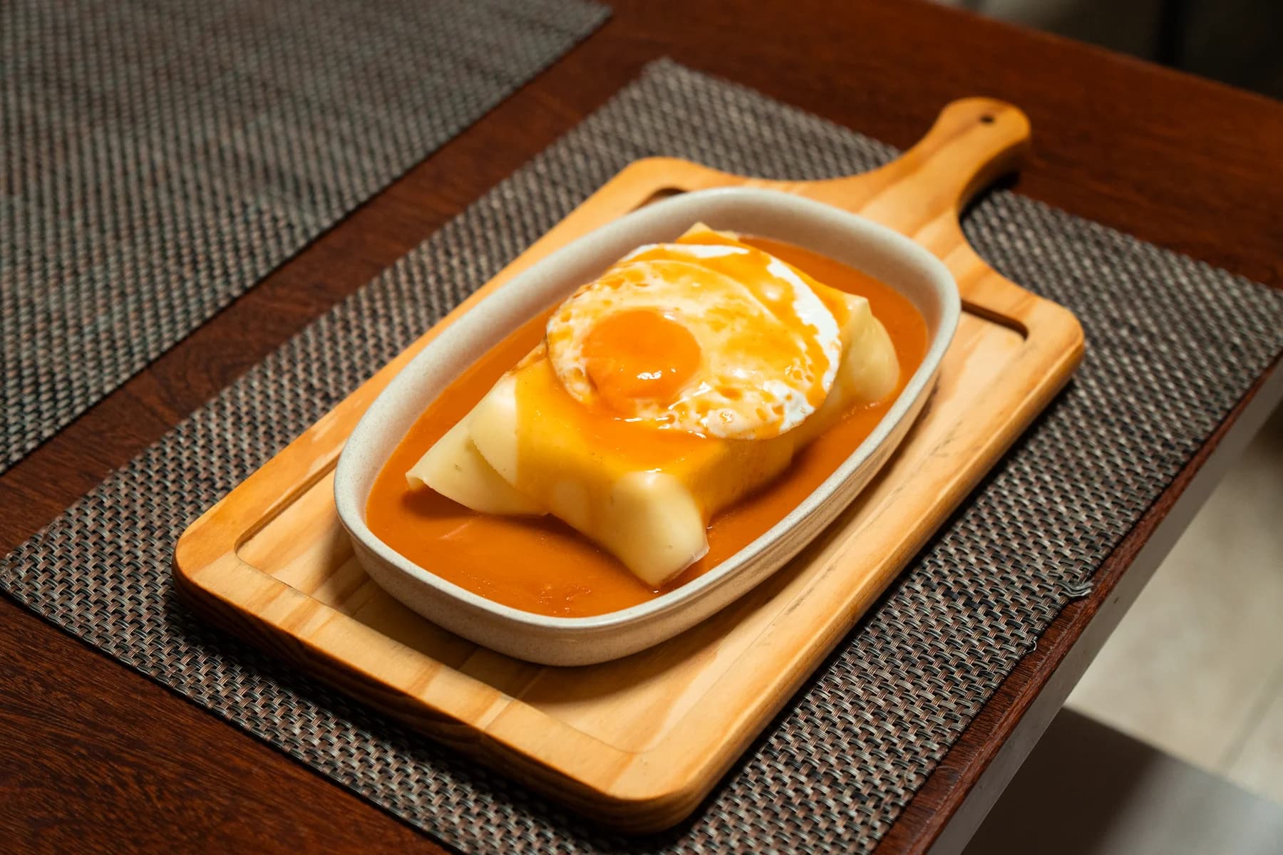 Francesinha with sauce and egg on a wooden board